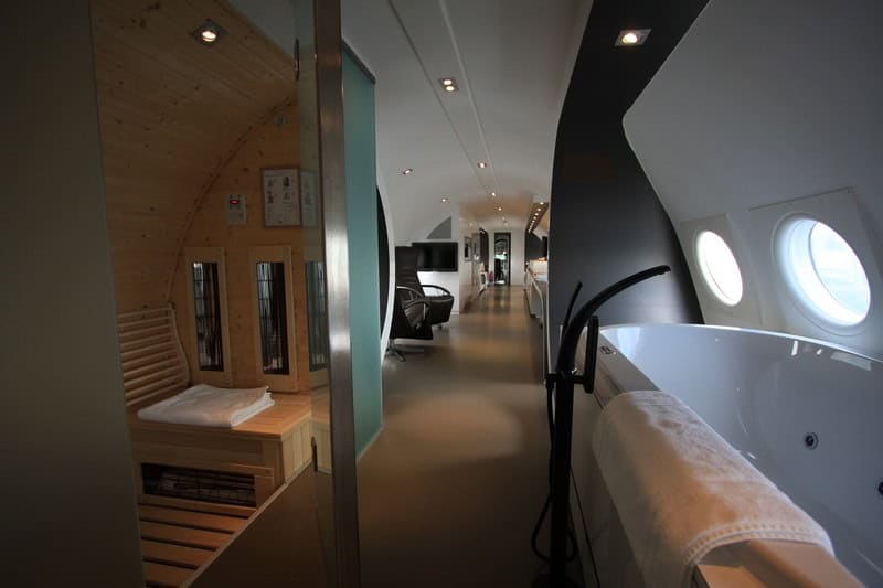 Infrared sauna with wood bench beside an oval white jacuzzi under porthole windows