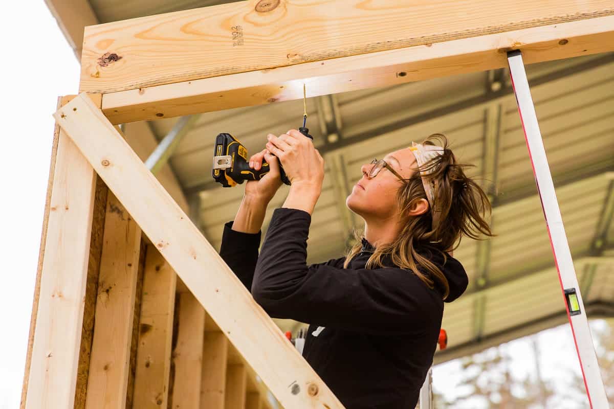 A student drives a screw into tiny-house wall framing during a Wild Abundance workshop