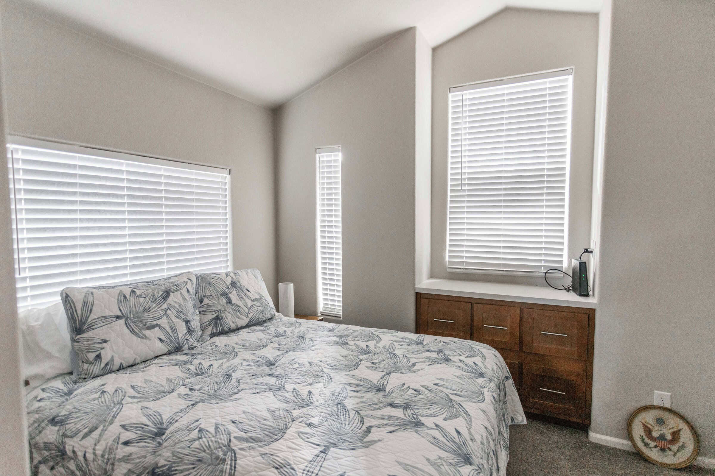Bedroom with a floral quilt, three windows, and a dresser under the right window