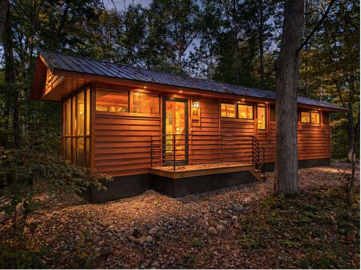 Woodland cabin exterior with warm wood lap siding and a metal roof, lit warmly at dusk in the hardwood forest at Canoe Bay Village Lot 12