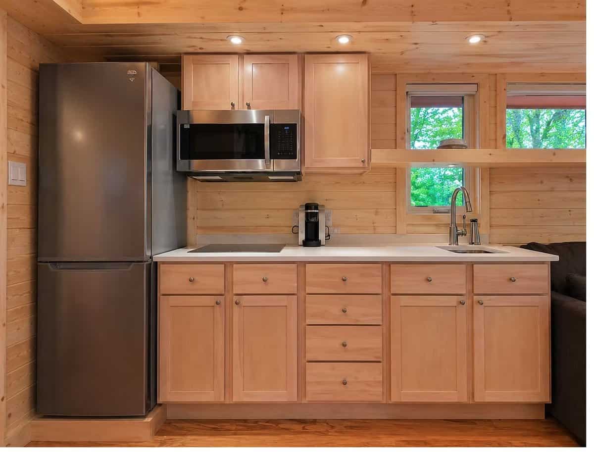 All-electric galley kitchen with maple cabinets, stone counters, induction cooktop, venting microwave, and a full-size refrigerator at the Woodland Lot 12