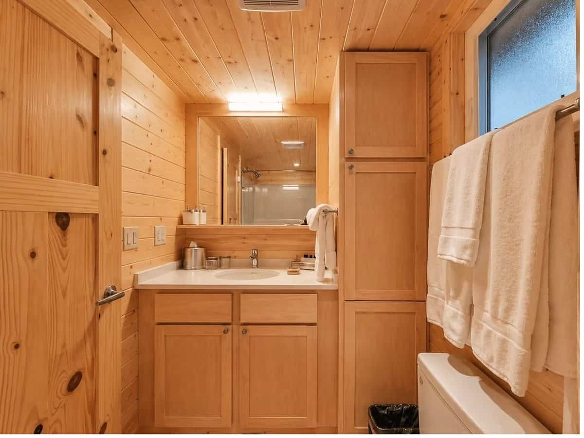 Bathroom with a stone-top maple vanity, framed mirror, and a tall built-in linen cabinet at the Woodland Lot 12