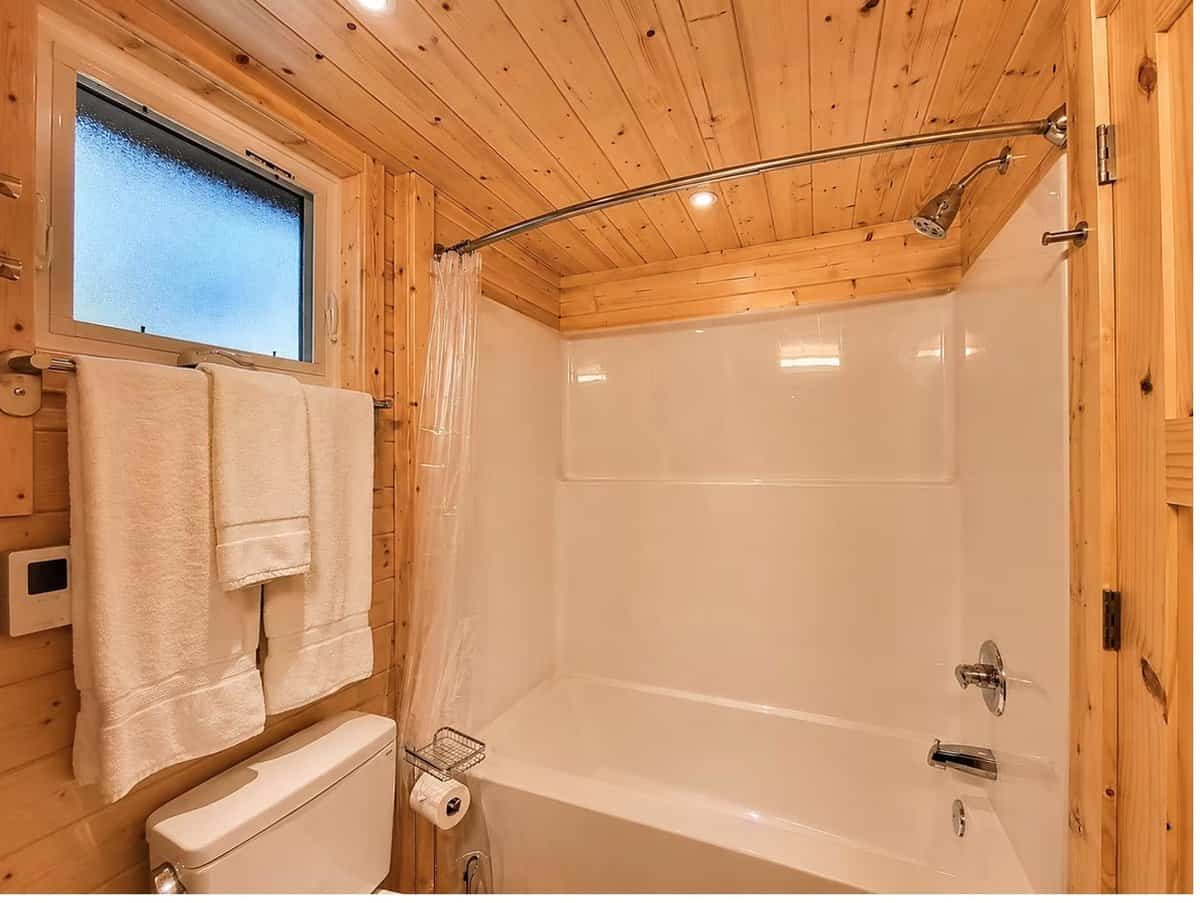Bathroom tub and shower combination with a curved curtain rod under a pine ceiling at the Woodland Lot 12