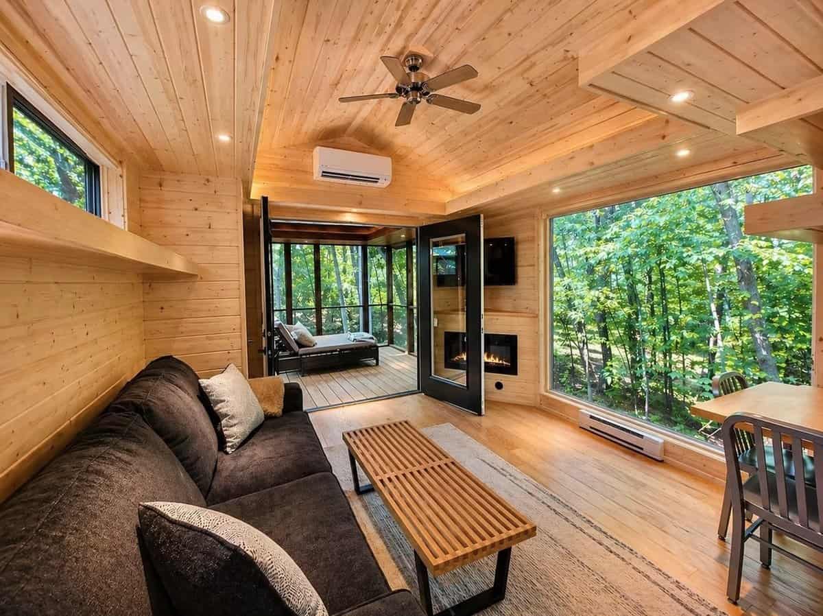 Pine-paneled living area with a charcoal sofa facing a glass fireplace and Smart TV, with a glass door to the screened porch at the Woodland Lot 12, Canoe Bay Village