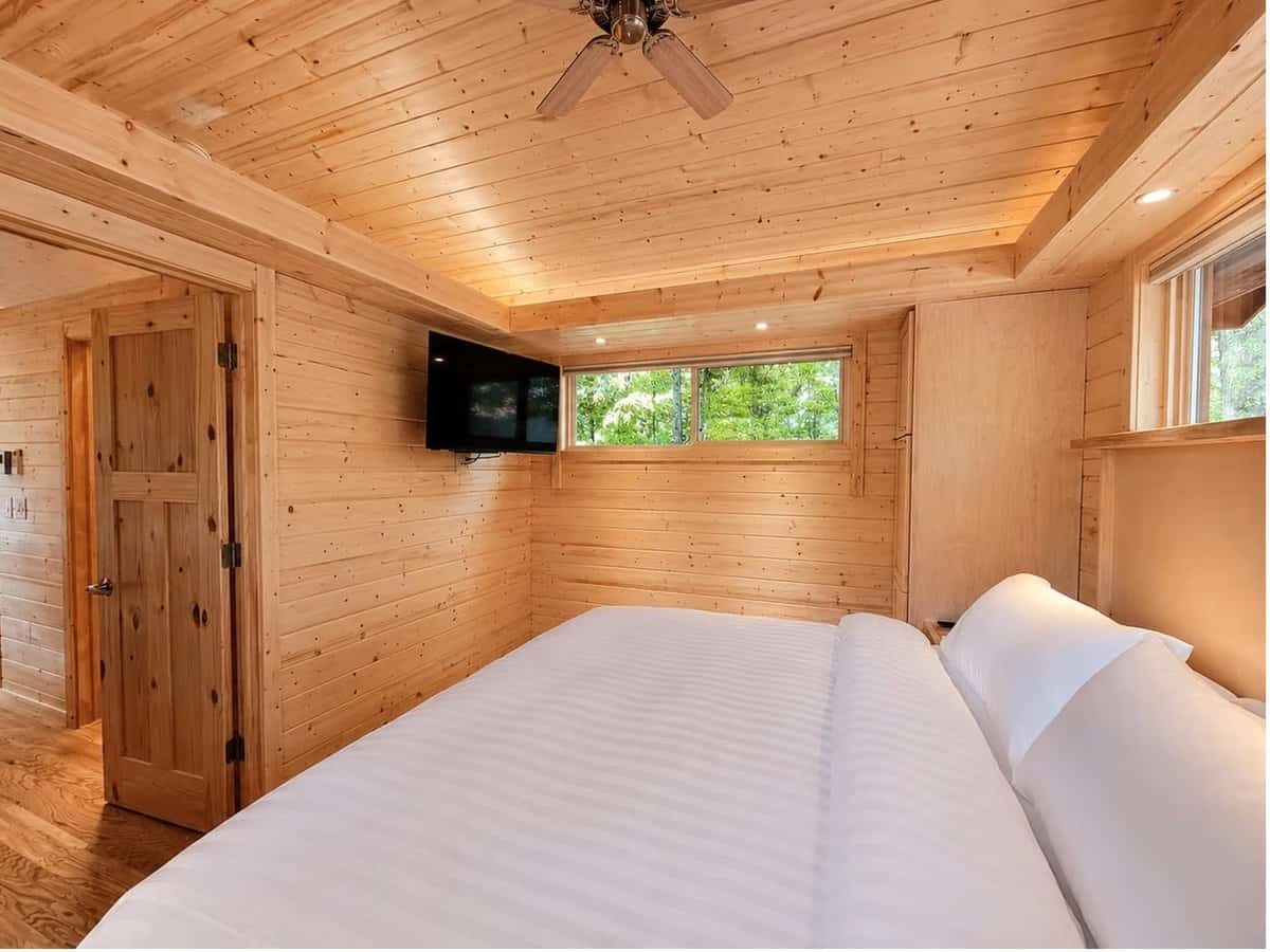 Angled view of the king bedroom with a wall-mounted Smart TV and pine paneling at the Woodland Lot 12
