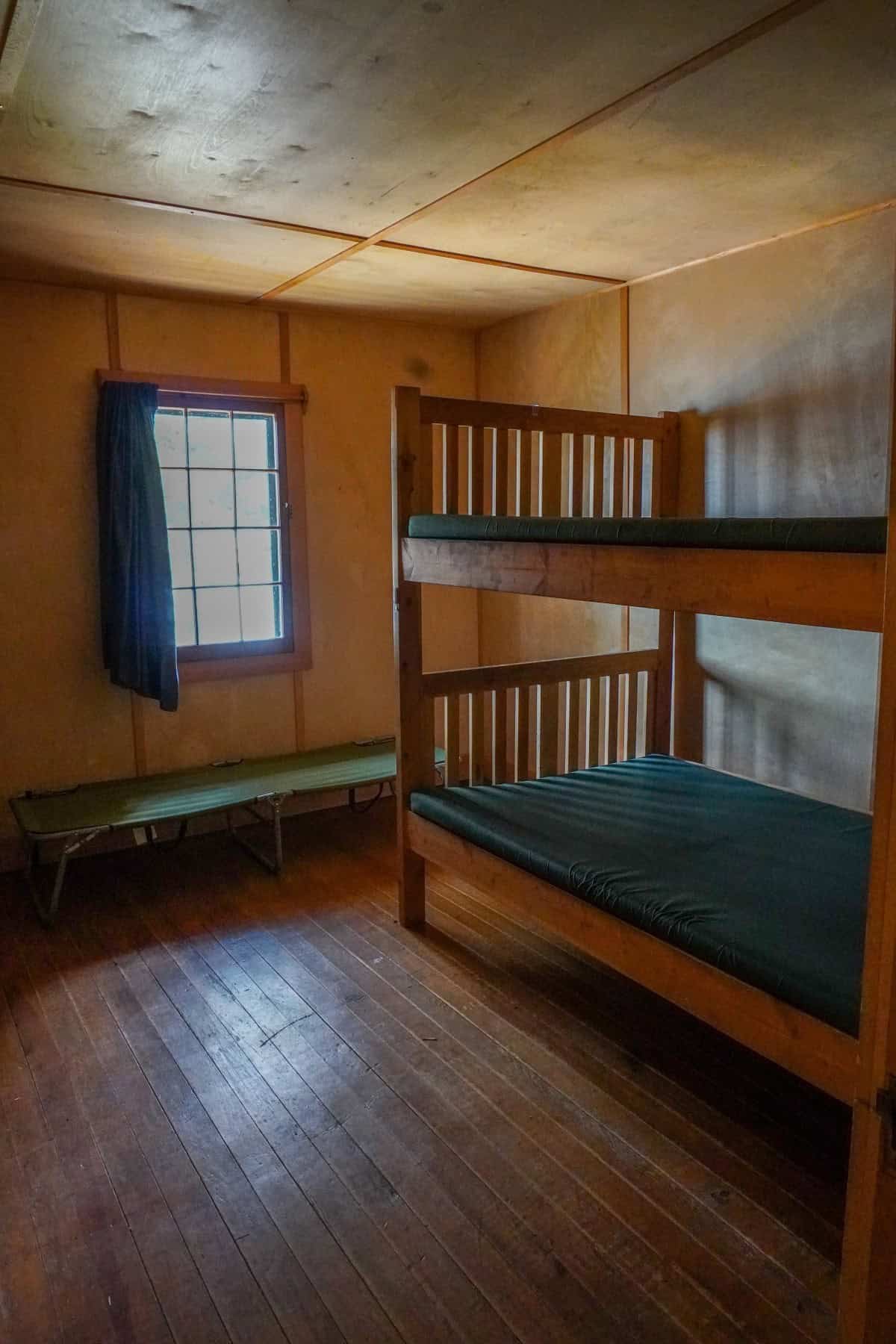 Bedroom with wooden bunk, green cot, and multi-pane window