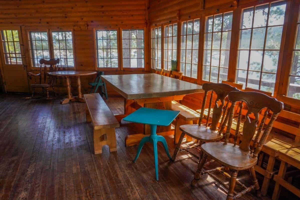 Living and dining room with trestle table, benches, multi-pane windows, and wood stove corner