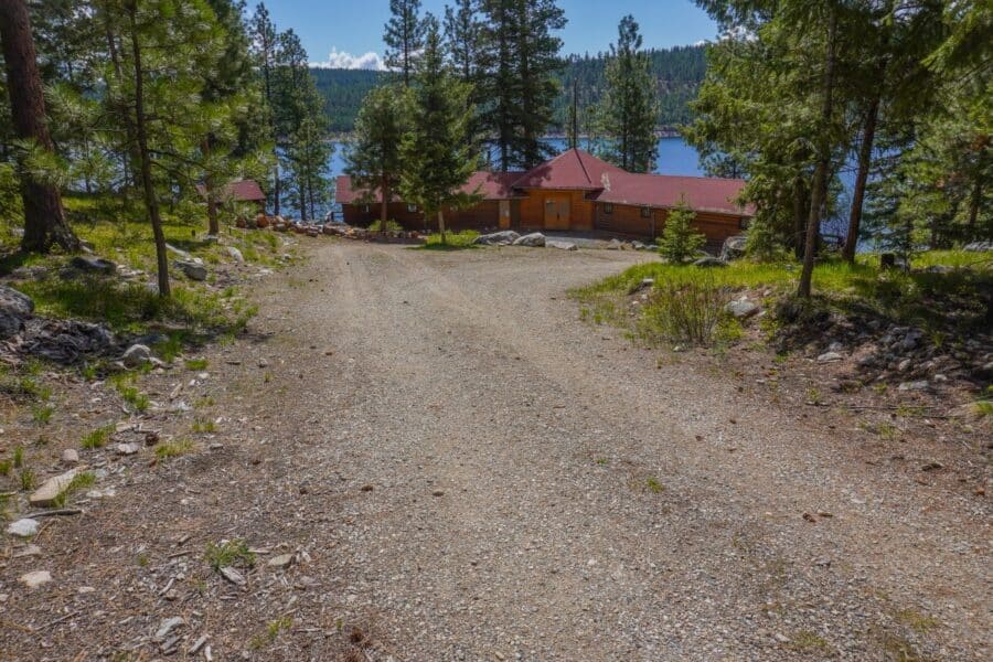 Elevated overview of red-roof log Woods Cabin on a gravel drive with Lake Como and forest behind