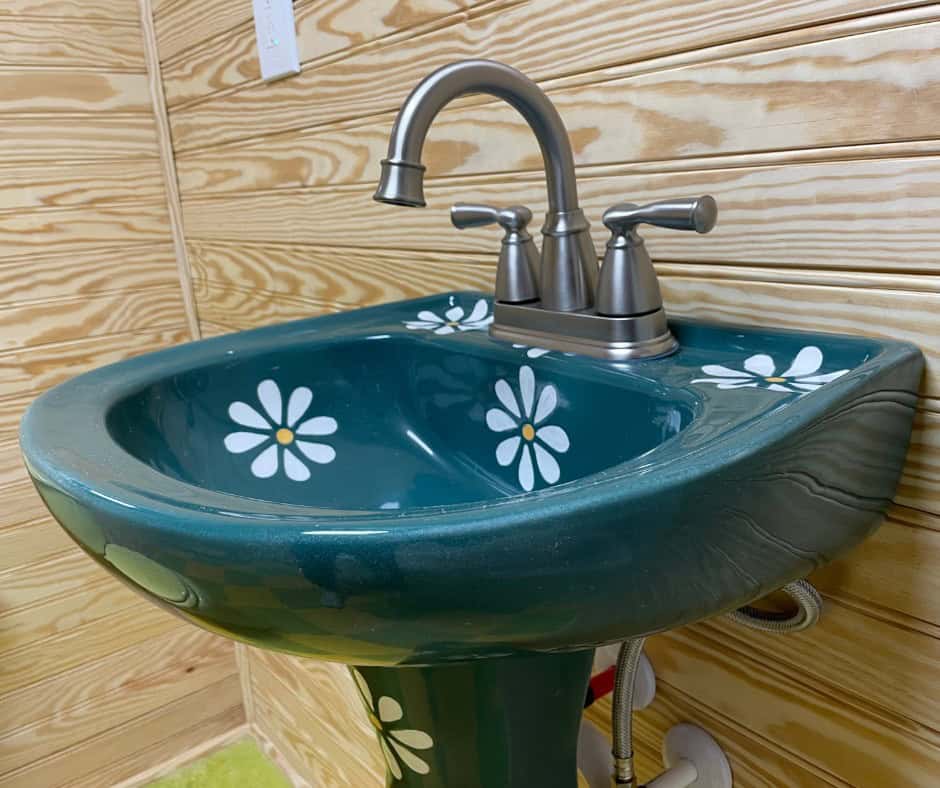 Dark green pedestal sink hand-painted with white daisies, with a brushed nickel faucet