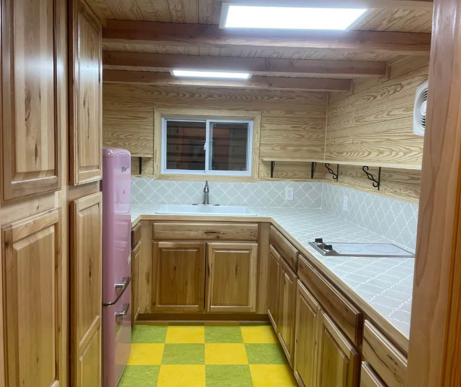 U-shaped kitchen with hickory cabinets, a tall pantry, a pink retro refrigerator, gray arabesque tile counters and backsplash, and a yellow and green checkerboard floor