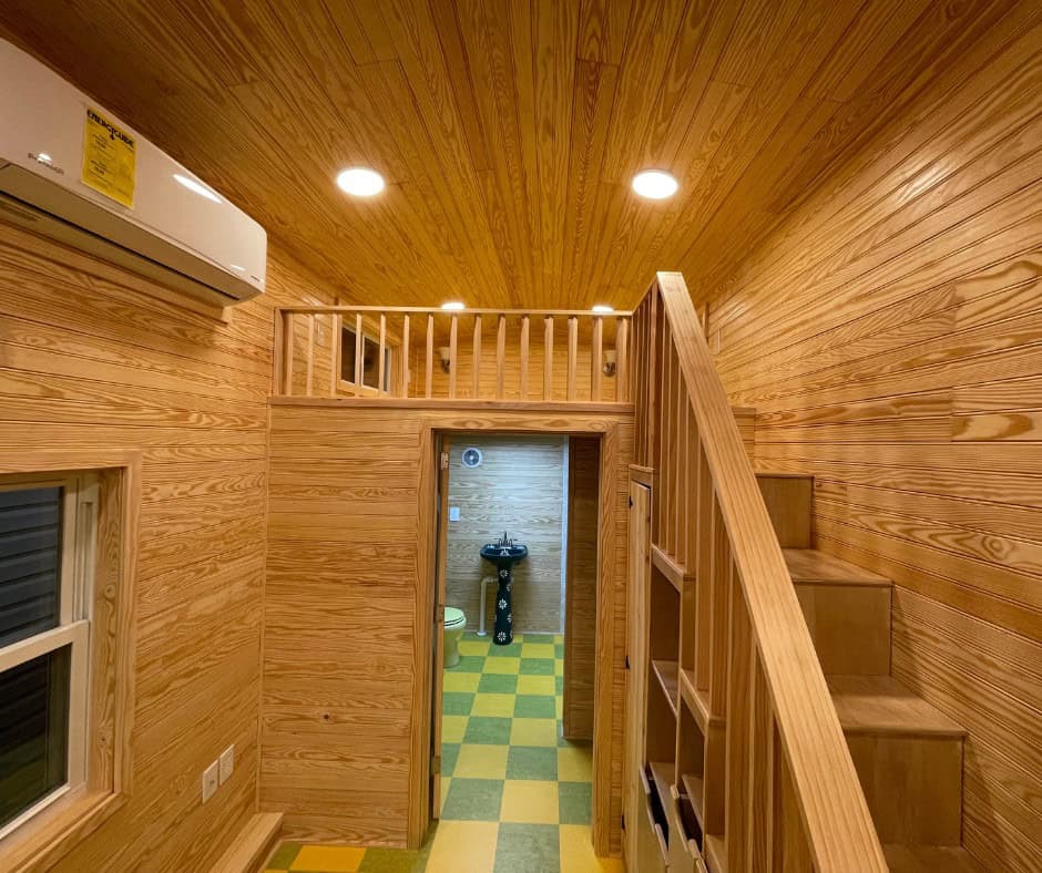 Loft railing above the bathroom doorway, with the stair rail at right and a green painted sink visible through the door