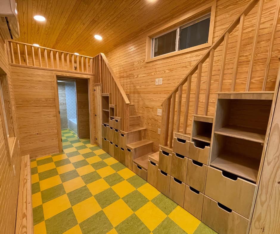 Wood staircase with built-in drawers and cubbies rising in two directions toward two lofts, over a yellow and green checkerboard floor