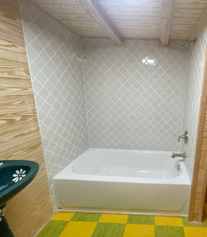 White bathtub and shower with a gray arabesque tile surround under wood ceiling beams