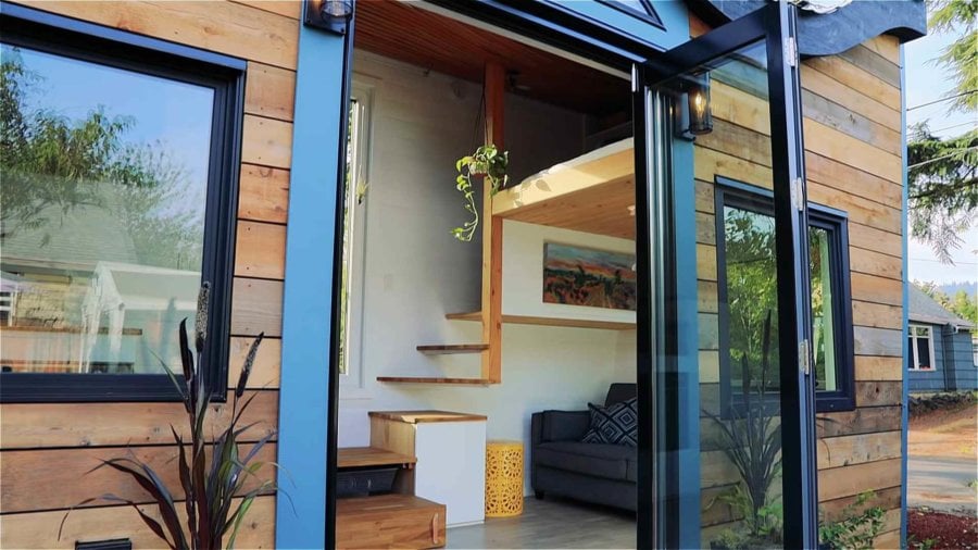 Looking through the wide-open glass entry door into the tiny house living room and floating stairs