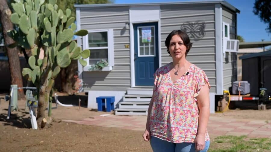 Woman standing outside a tiny house with cactus in the yard, embracing small space freedom.