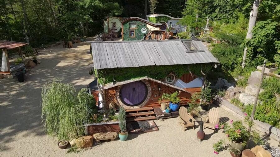 Charming tiny home inspired by fantasy design, nestled in lush greenery with outdoor seating and whi.
