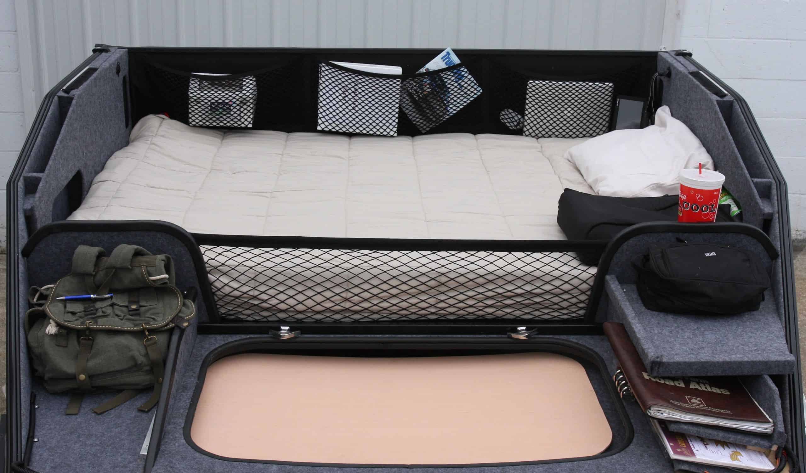 ZoomRoom over-the-cab sleeper interior with mattress, storage cubbies, and a rectangular floor portal — official ZoomRoom / Inoventure Industries photo