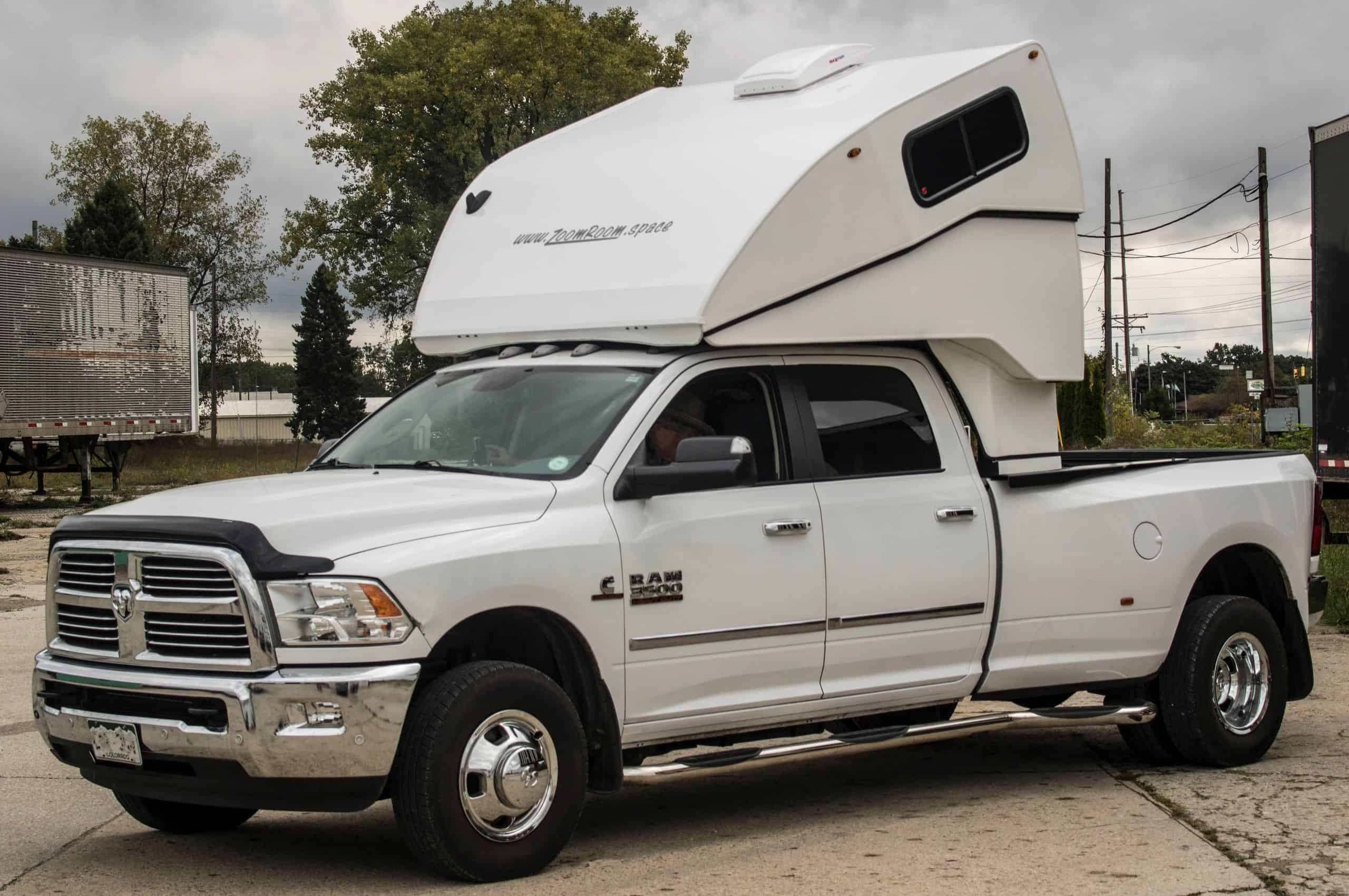 White pickup with a white ZoomRoom over-the-cab sleeper raised, zoomroom.space lettering on the nose — official ZoomRoom / Inoventure Industries photo